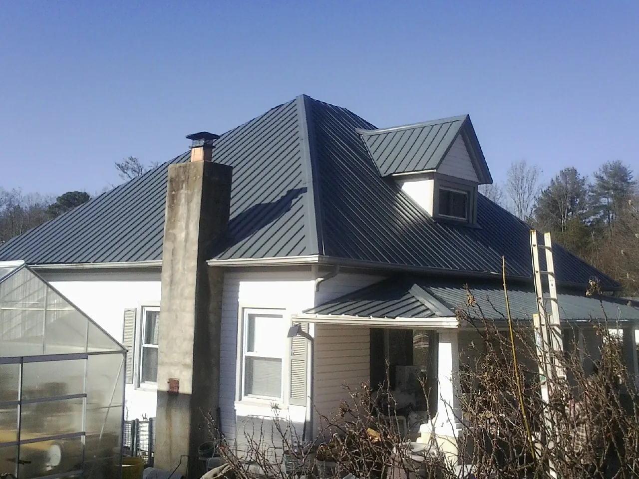 Dark blue standing seam metal roof on a white farmhouse with dormer — Slate & Tile Roof Repair by Roofing Brothers in Fort Meade