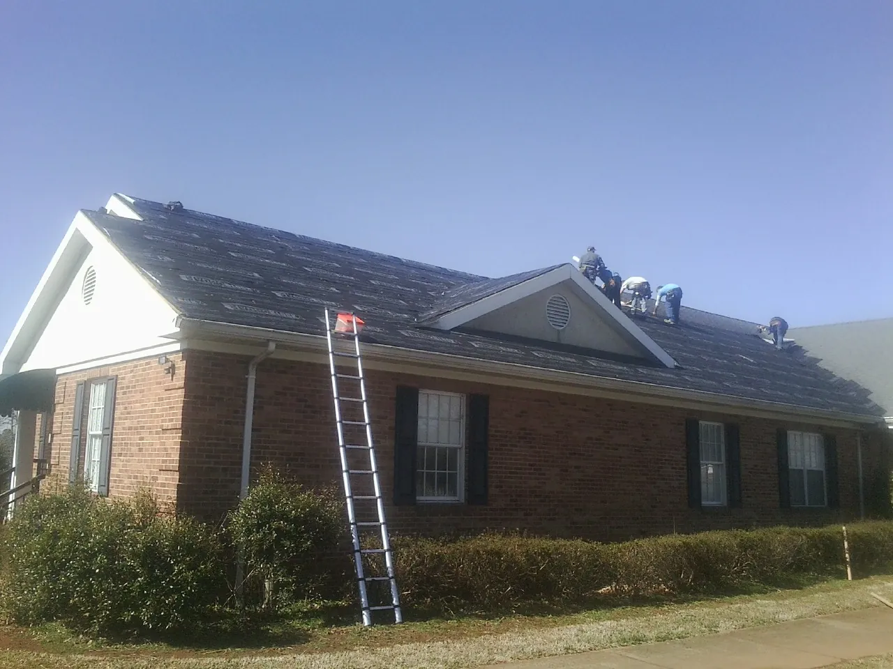 Crew tearing shingles off a brick ranch roof with a ladder set — Metal Roof Repair work by our crew in Fort Meade
