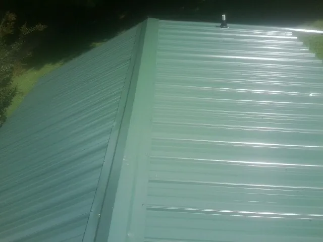 New green metal panels meeting at the ridge of a roof — Flat Roof Repair work by our crew in Fort Meade