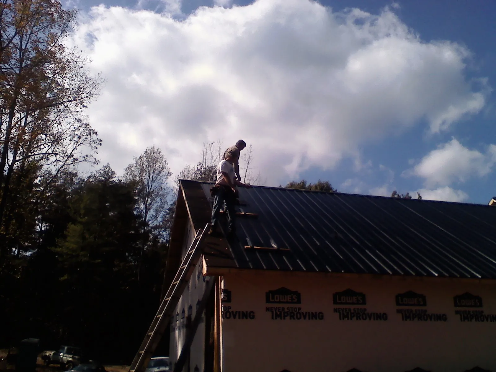 Roofer fastening dark metal panels high against a cloudy sky, from a Roof Inspection job in Fort Meade