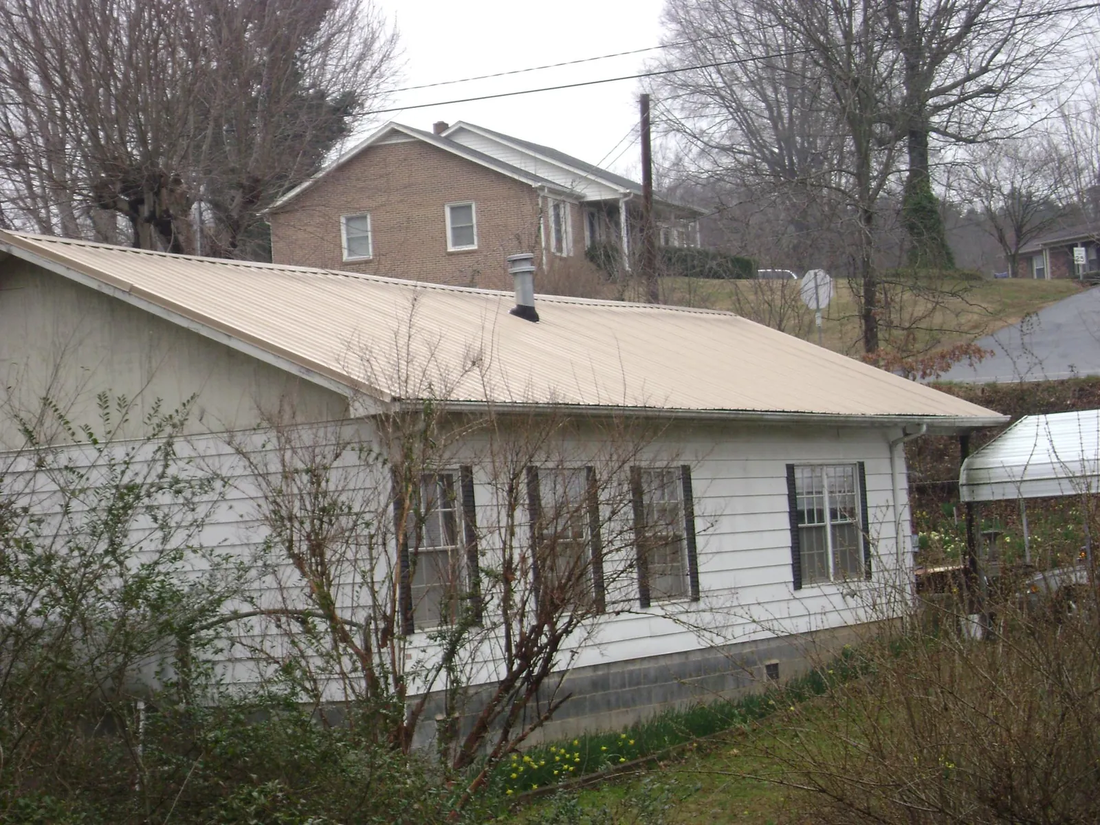 Tan metal roof on a white sided house set into a hillside — Commercial Roofing by Roofing Brothers in Fort Meade