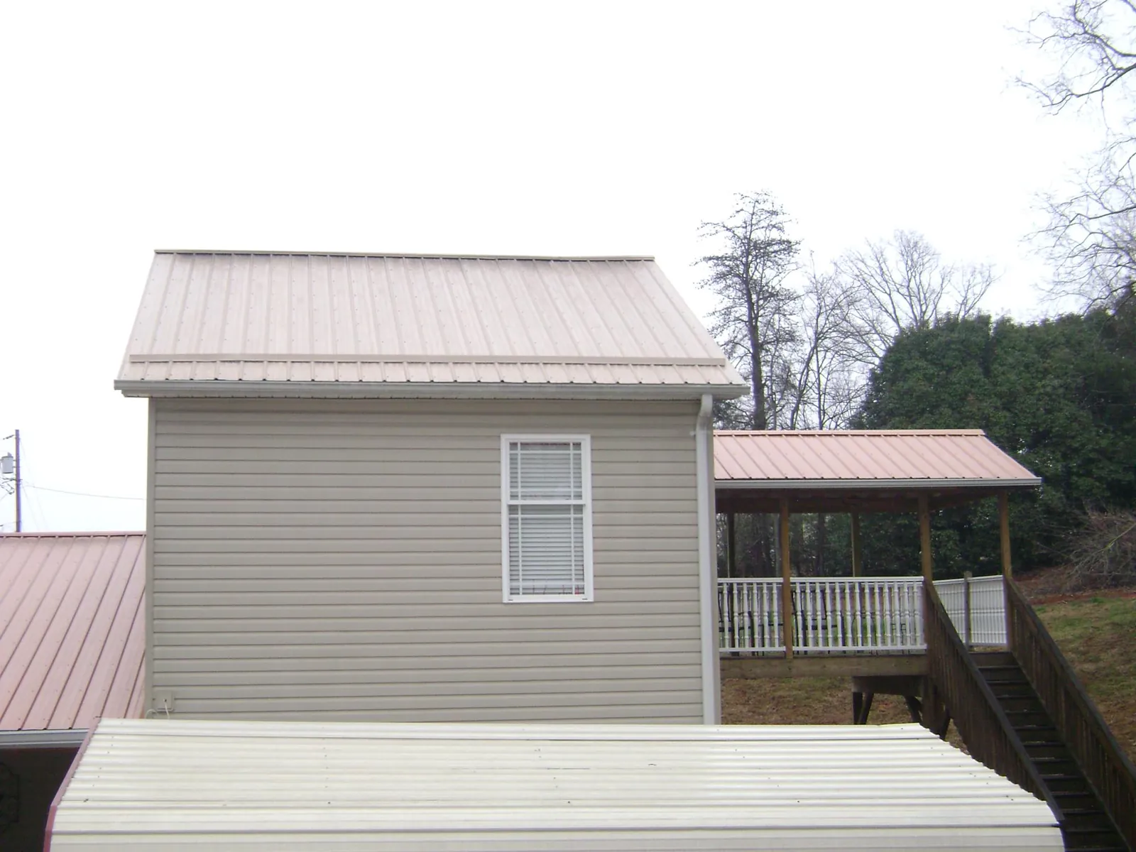 Tan metal roofs on a two story addition and attached porch, from a Roof Replacement job in Fort Meade